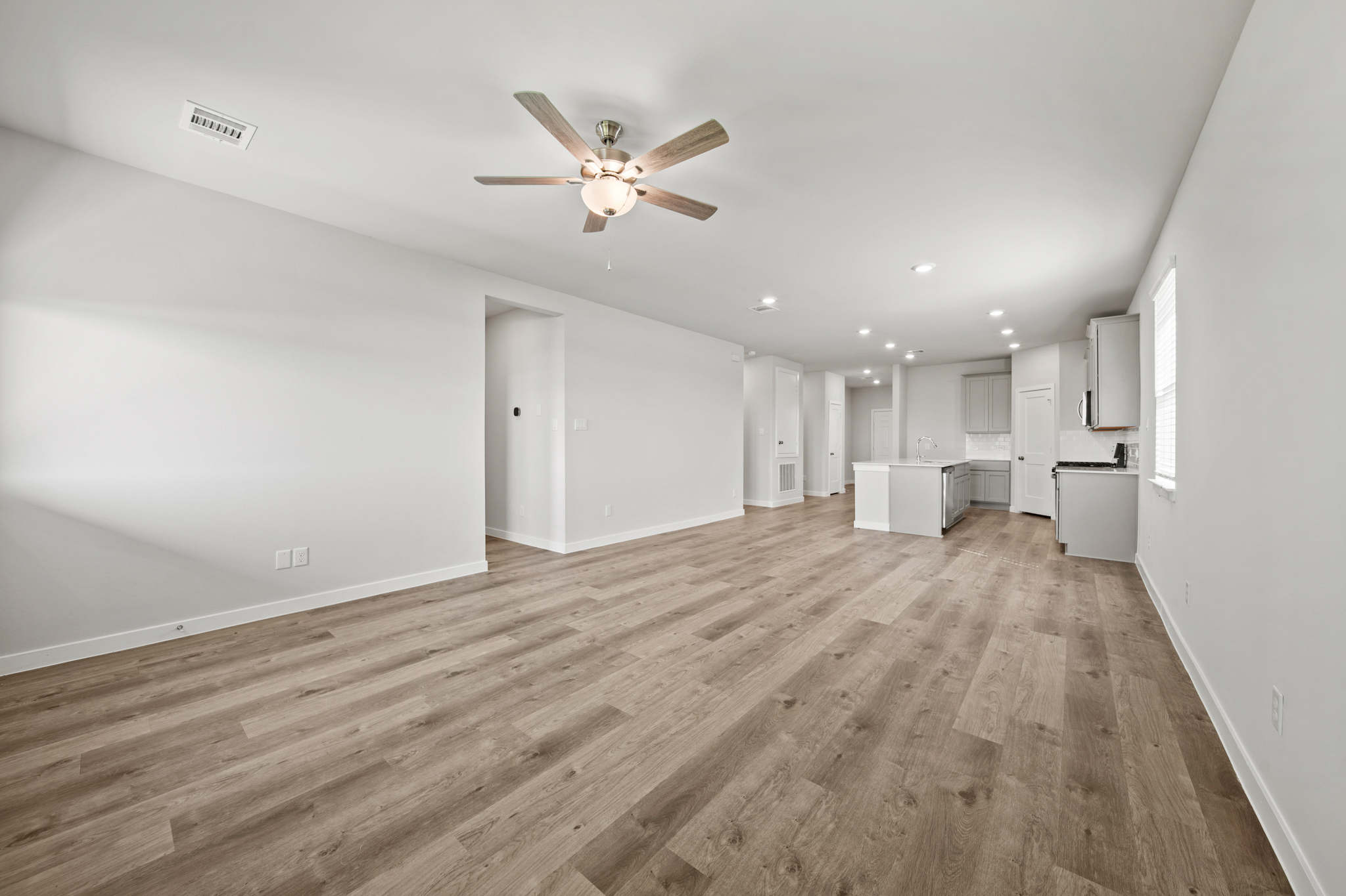 A large empty room with a ceiling fan and white walls.