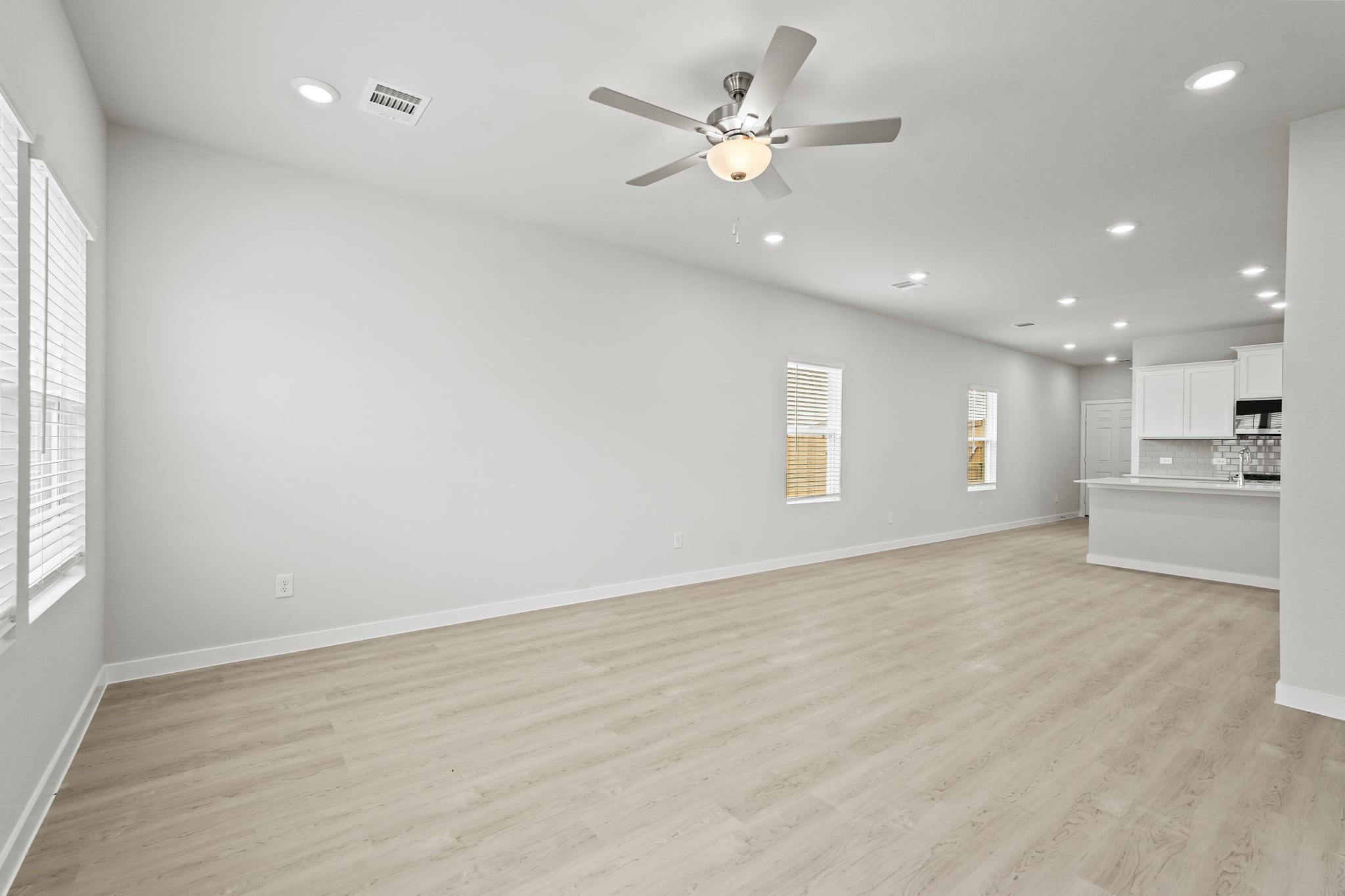 A large empty room with a ceiling fan and a wood floor.